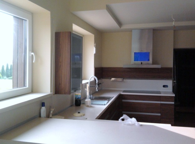 Nowoczesna kuchnia z zabudową karton-gips na suficie, drewniane szafki, biały blat i okap z niebieskim wyświetlaczem.